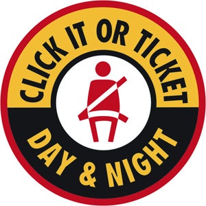 Circular seat belt enforcement campaign emblem reading 'CLICK IT OR TICKET' on a yellow top banner and 'DAY & NIGHT' on a black bottom banner, surrounding a central red icon of a person wearing a seat belt