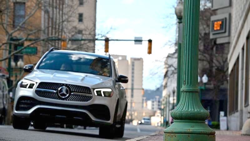 A silver Mercedes-Benz SUV driving on a city street, captured from a low angle with a green lamp post in the foreground.